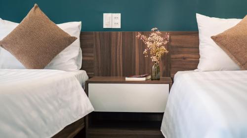 two beds with white sheets and a table with a vase of flowers at House of Pi Pleiku in Pleiku