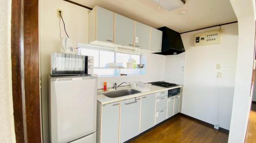 a small kitchen with white cabinets and a sink at 木の家ゲストハウス宇都宮2号館 in Utsunomiya