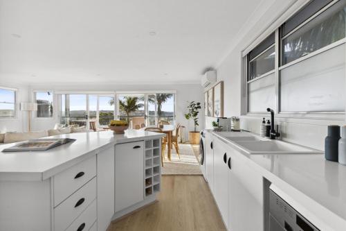 a kitchen with white cabinets and a living room at Chic Coastal 1-Bedroom Home with Balcony & BBQ in Deewhy