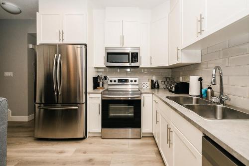 a kitchen with white cabinets and a stainless steel refrigerator at Modern suite near Airport Hospital Henday Town Ctr in Nisku