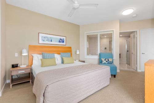a bedroom with a large bed and a blue chair at The Pool Resort Kingscliff - Private Apartments by Holiday Management Company in Kingscliff