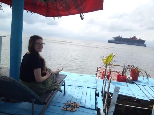 a woman sitting on a boat with a cruise ship in the background at Hotel Victoria s Beach House in Roatan