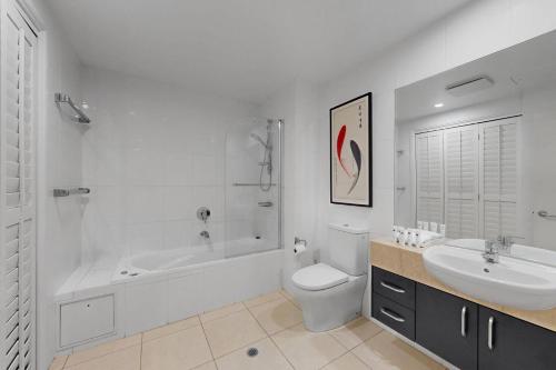 a white bathroom with a sink and a toilet and a tub at 11 Colonial in Noosaville