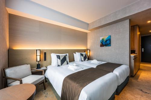 a hotel room with two beds and a chair at The Gate Hotel Fukuoka by Hulic in Fukuoka
