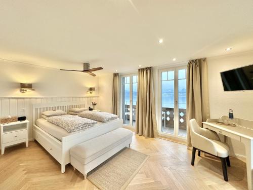 a white bedroom with a bed and a desk and a television at Boutique Hotel Niesenblick - direkt am Thunersee gelegen mit SELF CHECK IN & digitaler Rezeption in Oberhofen am Thunersee