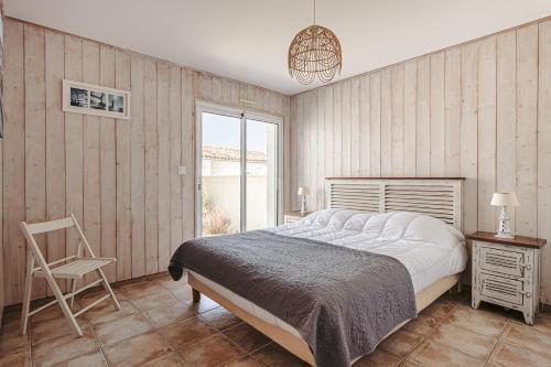 een slaapkamer met een bed, een stoel en een raam bij L'Avocette in Le Bois-Plage-en-Ré