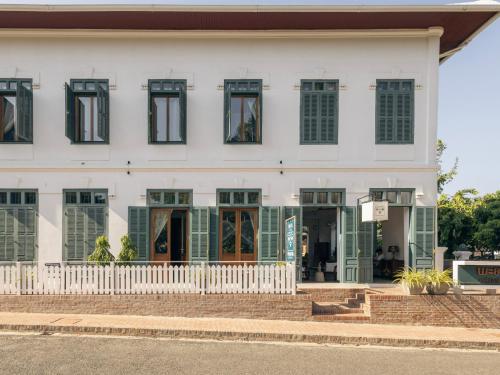 a white building with green shuttered windows at PHA NYA RESIDENCE in Luang Prabang