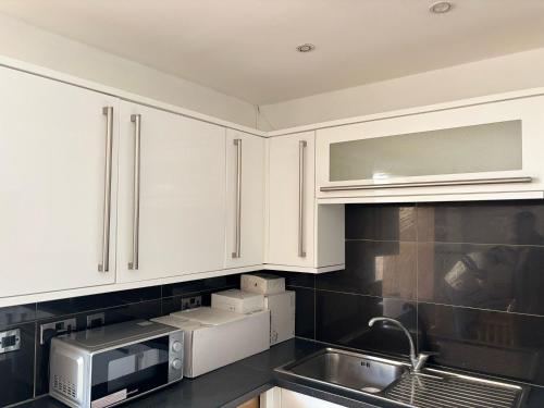 eine Küche mit weißen Schränken und einer Mikrowelle in der Unterkunft Modern 3 Bed Free Parking 10 mins walk to station in Dagenham