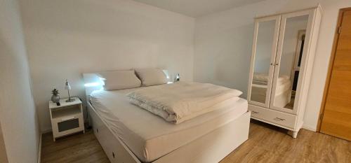 a small white bedroom with a bed and a mirror at Ferienwohnungen Das Finkhaus in Simonsberg