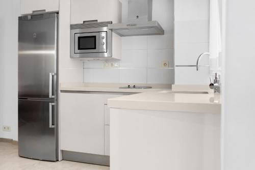 a white kitchen with a refrigerator and a microwave at Suites Campo del Príncipe by Maxi Hoteles in Granada