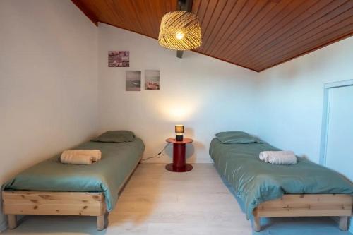 two beds in a room with a table and a lamp at Maison Caupos in Biscarrosse