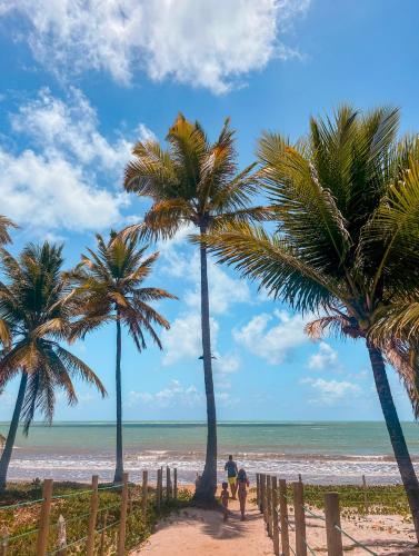 a group of people walking down a beach with palm trees at Villa Naluri - Casa Yodo - Apartamento 1 quarto em Japaratinga in Japaratinga