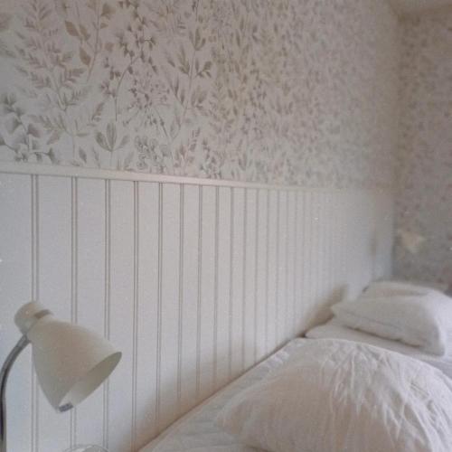 a white bedroom with a bed and a lamp at Borrgården Hostel in Ljusdal