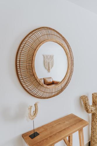 a rattan mirror hanging on a wall next to a wooden table at Shambhala Fuerteventura in Parque Holandes