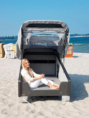 a woman sitting in a suitcase on the beach at Schlafstrankorb Nord Friends&Family, Meerwasserwellenbad in Eckernförde