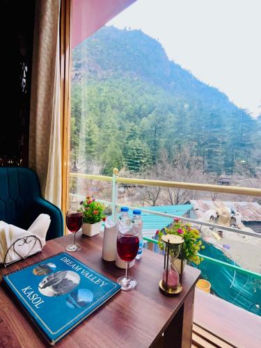 a table with two glasses of wine on a balcony at Hotel Brownie River View in Kasol