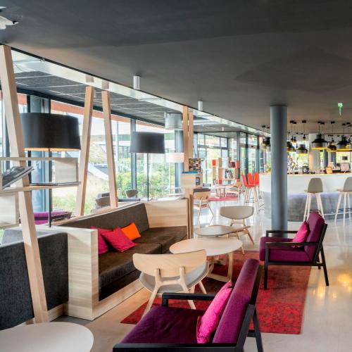 a lobby with tables and chairs in a building at Nomad Paris Roissy CDG in Le Mesnil-Amelot