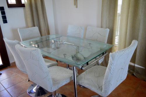a glass table with four white chairs around it at Malvazios Villas #3 in Gythio