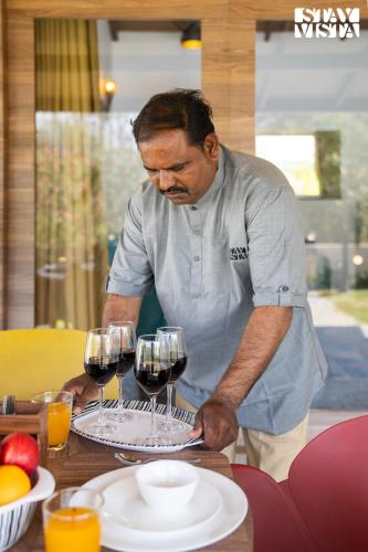 a man holding three glasses of wine on a table at StayVista at Asteria Enclave with WiFi, Pool, AC in Nashik