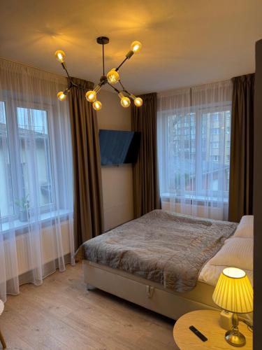 a bedroom with a bed with a chandelier and windows at DHARMA Stay Notaro apartamentai Self check-in in Telšiai