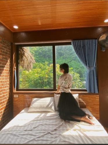 a woman sitting on a bed in front of a window at Tam Coc Moutainside Homestay in Ninh Binh