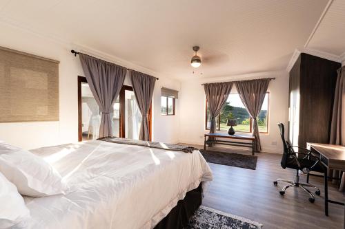a bedroom with a bed and a desk and windows at Fungamukaba Sanctuary in Mossel Bay