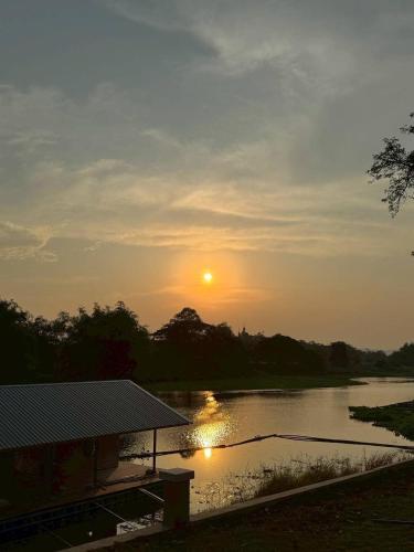 a sunset over a river with a pavilion in the foreground at สะแกกรัง ฮาเฟ่น โฮมสเตย์ Sakaekrang Haven Homestay in Uthai Thani