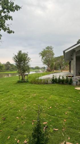 a yard with green grass and a house and a lake at สะแกกรัง ฮาเฟ่น โฮมสเตย์ Sakaekrang Haven Homestay in Uthai Thani
