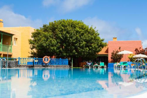 a pool at a resort with chairs and a tree at Apartamentos La Caleta in Los Cancajos