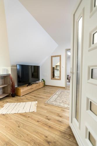 an open living room with a television and wooden floors at Mátravölgy Apartmanház in Pásztó