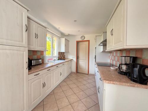 une cuisine avec des armoires blanches et un sol carrelé dans l'établissement Saint Ho Mer Maison lumineuse vue mer 8 pers 4 chambres 2 sdb 2 WC étage rénové en 2025 belle terrasse grand jardin clos parking 8 mn à pied petite plage grand jardin près de Port en Bessin, Bayeux et plage Omaha beach, à Sainte-Honorine-des-Pertes