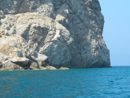 a large rock wall next to the blue water at Kalamos Due in Patti