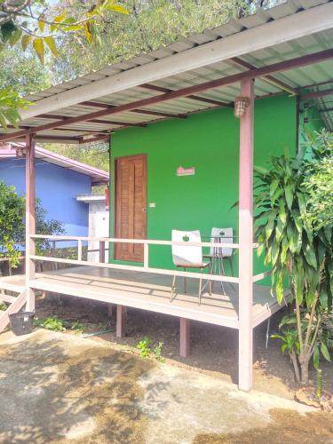 a green house with two chairs sitting on a porch at บ้านสวนนกโฮมสเตย์ OWLHOUSE in Ban Pong Pat