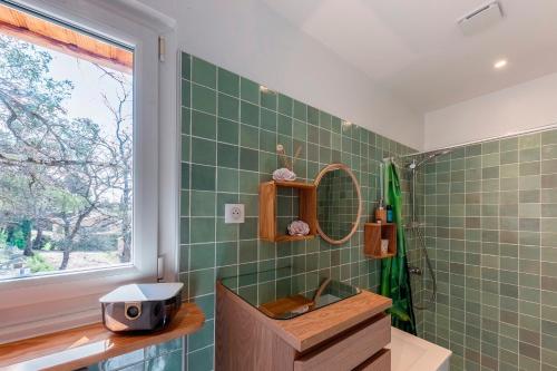 La salle de bains est pourvue de carrelage vert, d'un lavabo et d'une fenêtre. dans l'établissement Natura Provence, à Saint Antonin du Var