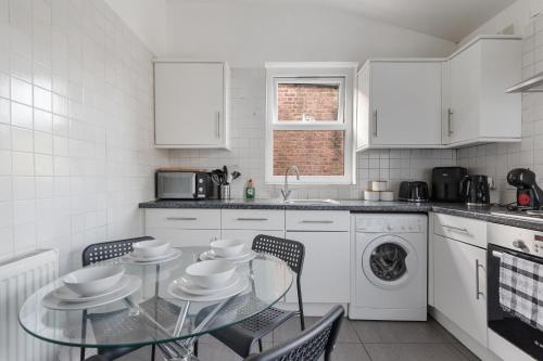 a white kitchen with a glass table and chairs at The Turnpike Residence - Free Parking in London