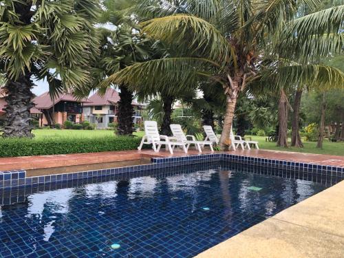 a swimming pool with two chairs and palm trees at The Chevalley Beach Resort in Satun