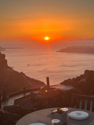 a sunset over the ocean with a table and the sun at Honeymoon Petra Villas in Imerovigli