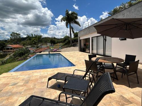 a patio with a table and chairs and a pool at Casa Pe na Agua Represa Igarata Piscina Climatizada in Igaratá