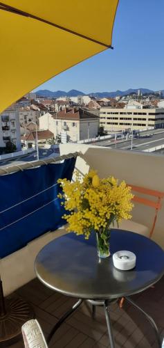 une table avec un vase de fleurs jaunes sur un balcon dans l'établissement Le lutetia 06, à Cannes