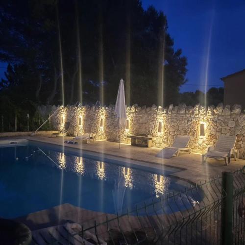 une piscine avec des chaises, un parasol et des lumières dans l'établissement La maison du soleil, à Mazan