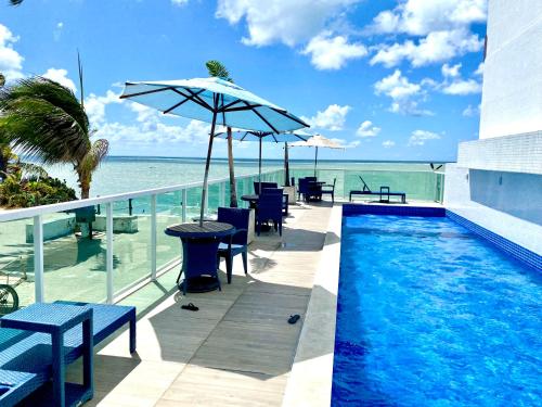 a swimming pool with chairs and an umbrella next to the ocean at Flamboyant Oceania Flats in João Pessoa