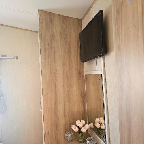 a flat screen tv hanging on a wall with flowers at Magic Caravan Camber Sands in Camber