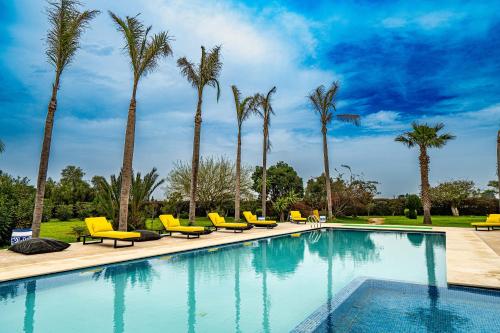 a swimming pool with yellow chairs and palm trees at Domaine Terra Cotta - Villa de luxe avec piscine sans vis-à-vis in Souk el Had