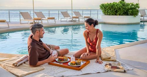 a man and woman sitting next to a pool with a tray of food at Grand Park Royal Puerto Vallarta - All Inclusive in Puerto Vallarta