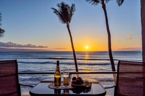 a table with a bottle of wine and a plate of food on the beach at Mahana 305 in Kahana