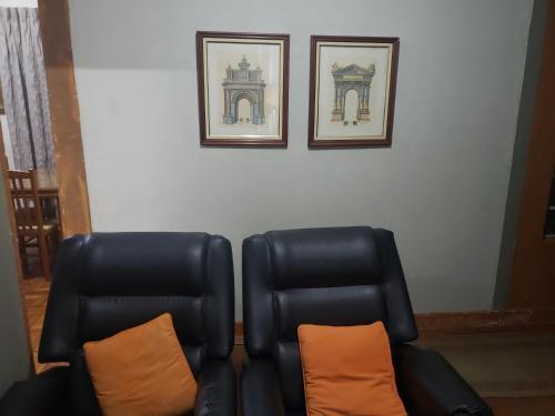a black leather chair with an orange pillow and two pictures at Guest House in Uberlândia