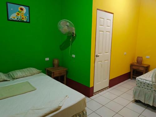 a green and yellow room with a bed and a fan at Cocos Hostel in Moyogalpa