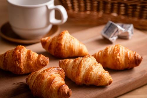 a group of croissants on a cutting board with a cup of coffee at Ooedo Onsen Monogatari Ureshinokan in Ureshino