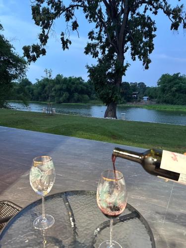 a bottle of wine is being poured into two wine glasses at สะแกกรัง ฮาเฟ่น โฮมสเตย์ Sakaekrang Haven Homestay in Uthai Thani