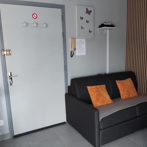 a black couch with two orange pillows in front of a door at Le repos d'Aubrac in Laguiole